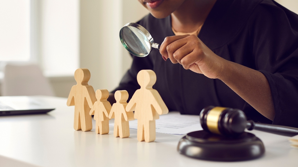 lawyer looking in magnifying glass at little mom, dad children figures on desk
